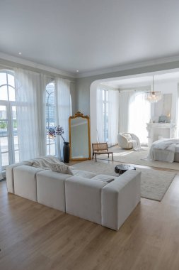 Büyük panoramik pencereli, güneşli, rahat, parlak bir daire. Beyaz, bej renkli, şömineli ve koltuklu bir yatak odası. Kütük sehpası ve büyük beyaz kanepesi olan şık bir oturma odası.