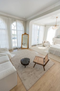 Büyük panoramik pencereli, güneşli, rahat, parlak bir daire. Beyaz, bej renkli, şömineli ve koltuklu bir yatak odası. Kütük sehpası ve büyük beyaz kanepesi olan şık bir oturma odası.