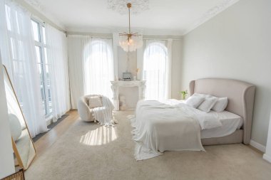 Güneşli, panoramik pencereli, yumuşak, parlak bir daire. Yumuşak bej renkte bir yatak odası şöminesi, şık bir döşemesi ve yatağı var.