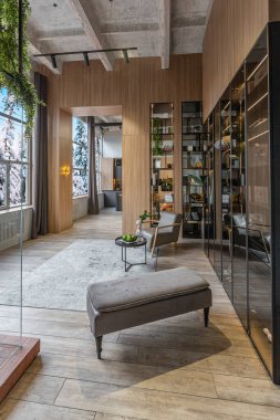 Yüksek tavan tavanı, ahşap dekorasyonu ve gri duvarları olan büyük, modern, geniş bir dairede ışık saçan şık bir soyunma odası.