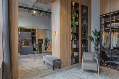 Yüksek tavan tavanı, ahşap dekorasyonu ve gri duvarları olan büyük, modern, geniş bir dairede ışık saçan şık bir soyunma odası.