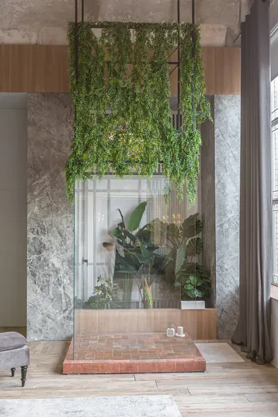 stock image A jungle-styled glass separate shower in greenery in a huge modern spacious apartment with high loft-style ceilings, wooden trim and gray walls