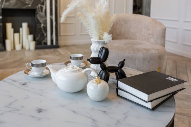 Modern bir oturma odasındaki çay masasına yakın çekim. Mermer şöminesi olan ve gündüz vakti yanında kimse olmayan şık, parlak bir dairede.