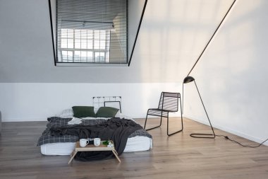Minimalist stil. Tavanda penceresi ve güneş ışınları olan, bembeyaz, sade yatak odası.