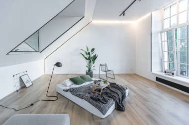 Minimalist stil. Tavanda penceresi ve güneş ışınları olan, bembeyaz, sade yatak odası.