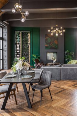 Karanlık, vahşi bir iç mekanda, panoramik pencereli tarihi bir malikanede lüks, şık bir yemek masasının yakın çekimi. Gri yeşil duvarlar ve kahverengi parke