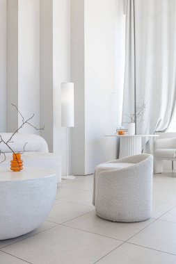 Modern, saf, beyaz bir iç tasarım. Yumuşak stil mobilyaları olan şık bir oturma odası. Geniş pencere çerçevesi gün ışığında sakin bir atmosfer yaratıyor.