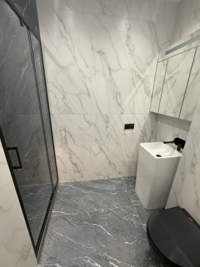 Şık bir banyo mermer duvarlar ve parlak bir tasarım sergiler. Yumuşak ışıklandırma ayrıntıları vurgular, havlular ise duşun yanında düzgünce asılı, sofistike atmosferi geliştirir..