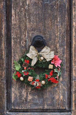 Eski ahşap bir kapının üzerinde Noel tacı çelengi. Noel boyunca geleneksel ev dekorasyonu, dikey