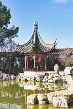 Chinese gazebo in garden with Chinese red traditional lanterns on the shore of the sacral carp pond. Traditional Chinese red lanterns are hung in gardens during celebrating Chinese New Year