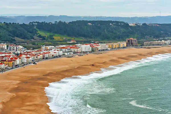 Geniş kumlu sahil şeridi boyunca sıralanmış kırmızı kiremitli çatıları olan Nazare kıyı kasabası rüzgar sörfü için en popüler yerdir.