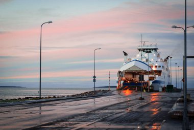 Yükleme sırasında rıhtımda konuşlanmış yolcu feribotu, yumuşak pastel renklerle, sakin günbatımı gökyüzünün altında.
