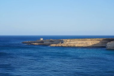 Sakin mavi Akdeniz 'e uzanan geniş bir sahil kayalığı berrak güneşli gökyüzünün altında sakin bir manzara.