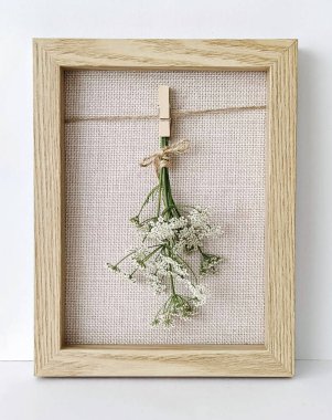 Small dried flowers tied with twine displayed in a wooden frame over textured canvas clipart