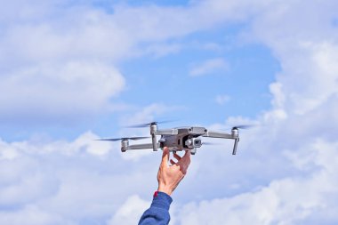 Parlak bulutlu gökyüzüne uzanmış modern kuadkopter drone 'u tutan kişi. İHA Elle Fırlatılıyor