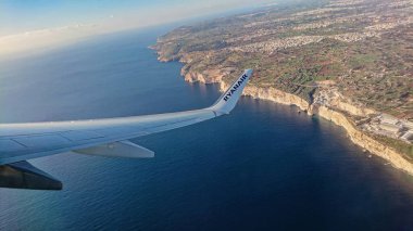 Ryanair uçak kanadı, Malta kıyısı uçurumunda süzülüyor, uçuş sırasında derin mavi deniz ve açık gökyüzünü gösteriyor: Luqa, Malta 9.01.2020