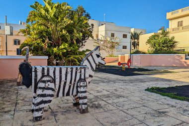 Kırsal ahşap zebra yapısı, yerleşim alanındaki yemyeşil bitkilerle çevrili, yıpranmış oyun bahçesinde duruyor.