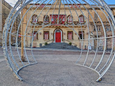 Christmas light installation opposite historic Maltese building adorned with festive wreaths and red accents, creating holiday scene clipart