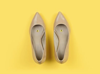 Pair of beige classic womens shoes with pushpin on yellow background. Pranks and tricks concept for April fools day with copy space clipart