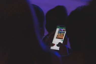 Mavi ve mor ışıkla aydınlatılmış loş bir ortamda akıllı telefonunu kullanan bir kadın. Xghajra, Malta - 28 Haziran 2019 