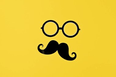 Bıyık ve gözlük silueti koyu sarı yüzeyde, oyuncu bir stil sergiliyor, komik markalaşmaya oyuncu bir yaklaşım, yaratıcı kimlik potansiyelinin oyuncu bir hatırlatıcısı.