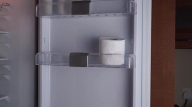 Buzdolabının içinde tuvalet kağıdı olan eller alışılmadık bir depolama numarasını gösteriyor. Tuvalet kağıtları ürünleri nem ve kötü kokulardan korur. Ev fikri konsepti için yeni bir can kurtarma deposu