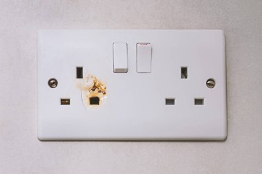 Closeup of burnt British wall outlet with melted edges. Burnt evidence of electrical meltdown, and burnt sign of potential fire risk, calling for immediate repair to ensure safer home environment clipart