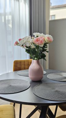 Çiçekli pembe vazo rafine yemek alanının altını çizer, yumuşak pastel paleti yansıtan çiçekler, modern iç atmosferi yükselten çiçekler, marka tasvirleri ve editoryal kavramlara hitap eder.