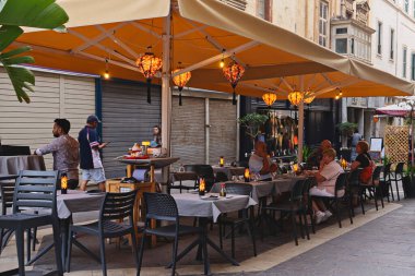 Açık hava restoranındaki akşam yemeği sahnesi sıcak ışıklar altında toplandı: Valletta, Malta - 14.05.2024
