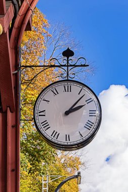 Street clock in autumn colors reminds of symbolizing seasonal transition in Europe. Clock with classic roman design and vintage street style