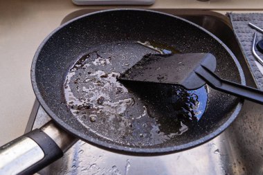 Lavaboda sıcak yağlı ve yağlı tencere, yakınlarda siyah spatula, temizleme işlemine başla, mutfak konseptini temizle.
