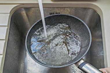 Musluğun altında su akıntısı ve köpükle sıcak yapışmaz tava, yanmış parçalar yıkayıp temizleme, aktif durulama adımı