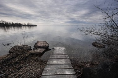 In the image, a lake with a dock is depicted in black and white, capturing a serene natural landscape with water, sky, clouds, and trees clipart