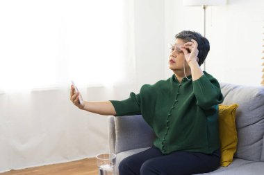 Uzun görüşlü yaşlı bir kadın kitap okumaya çalışıyor, evdeki kanepede oturuyor..