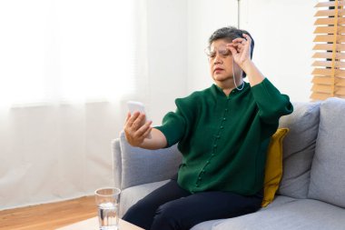 Uzun görüşlü yaşlı bir kadın kitap okumaya çalışıyor, evdeki kanepede oturuyor..