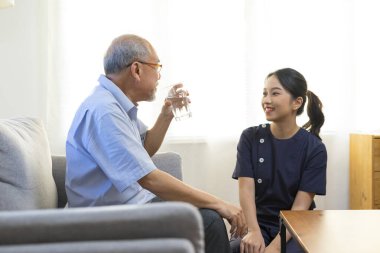 Gülümseyen hemşire huzurevindeki yaşlı Asyalı adama ya da huzurevindeki huzurevine su veriyor..