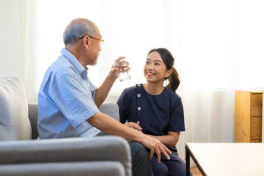 Smiling nurse giving glass of water to senior asian man in nursing home or assisted living facility. clipart