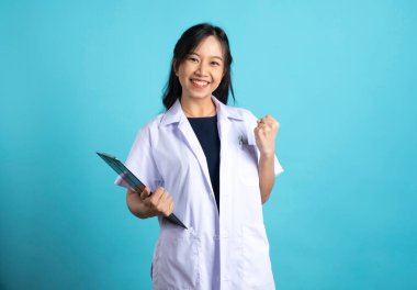 Genç mutlu bayan Aisan doktor ya da hemşire elinde bir pano ile mavi arka plana yumruk hareketi yapıyor. 