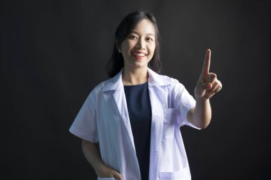 Stüdyoda gülümseyen Asyalı kadın doktorun siyah arka planı işaret ettiği bir fotoğraf.