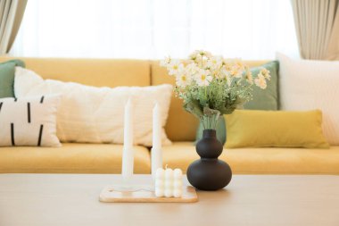 Ahşap masada mumlar ve vazolarla rahat bir ev. Yeşil beyaz yastıklı sarı kanepe