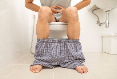 Asyalı adam klozette otururken ishal oluyor. Mide ağrısı, banyoda kabızlık..