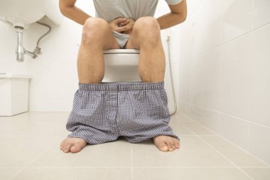 Asyalı adam klozette otururken ishal oluyor. Mide ağrısı, banyoda kabızlık..