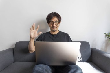 Genç Asyalı adam dizüstü bilgisayar kullanıyor.