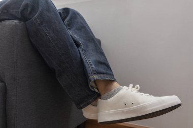 Adam oturma odasında spor ayakkabılarıyla kanepede oturuyor, yakın plan.