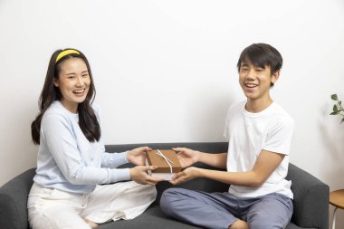 Genç Asyalı çift evde gülümseyerek hediye paketi tutuyorlar.