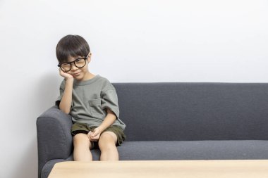 Küçük çocuk kanepede oturuyor ve bir şeye bakıyor.