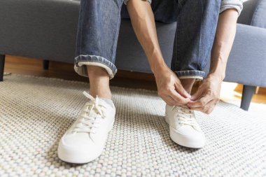 Kanepede ayakkabılı bir adam oturuyor.