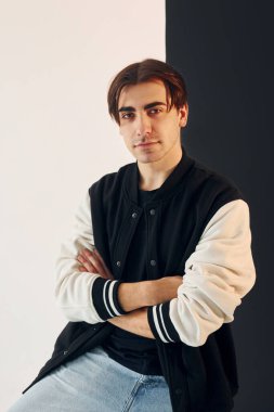 Looking into the camera. Young man is in the studio with white and black walls.