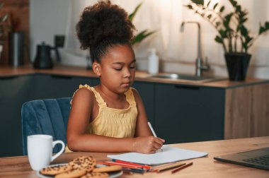 Çizim için dizüstü bilgisayar ve kağıtla. Gündüz vakti evde rahat giyinen sevimli siyah kız var..