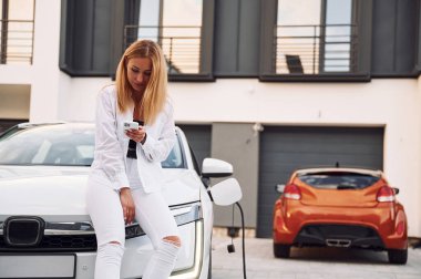 Evin yakınına. Beyaz elbiseli genç bir kadın gündüz vakti elektrikli arabasıyla geliyor..